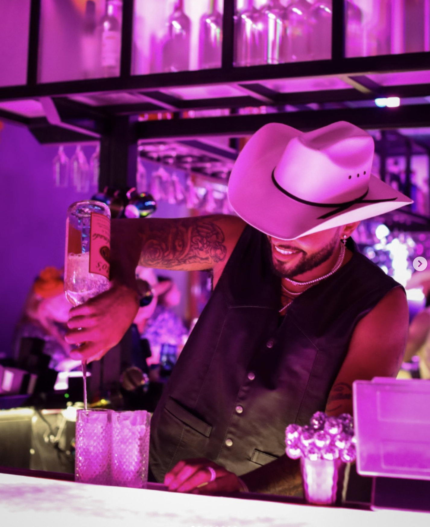 Bartender in a cowboy hat performing a long pour at Lola’s Liquors under magenta light