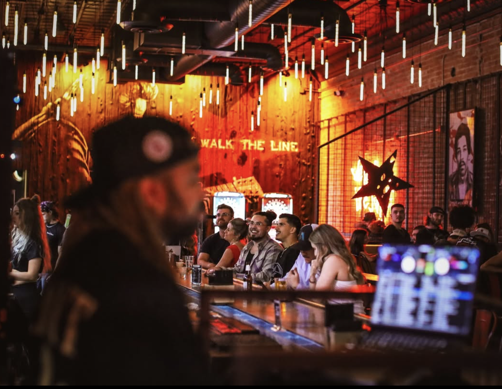 Crowd under icicle pendants with Walk the Line neon at Rebel & Rogue